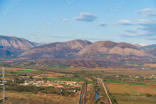 Saranda, Albania - August 26, 2025: High angle panoramic view of a river valley with agricultural fields, villages and massive mountains during sunset