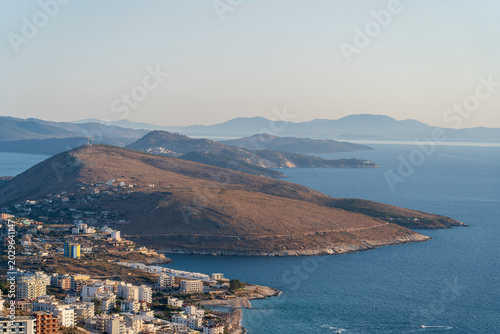 Saranda, Albania - August 24, 2025: High angle view of a suburban coastal area with hotels and residential buildings built on the slopes of a dry hill by the Ionian sea