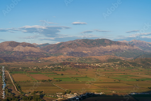 Saranda, Albania - August 26, 2025: Wide high angle view of agricultural fields in a vast valley surrounded by mountain ranges under a blue sky at sunset