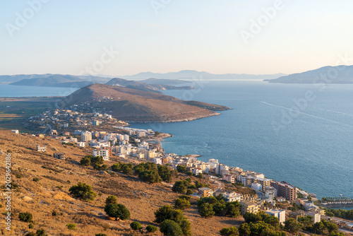 Saranda, Albania - August 26, 2025: Wide panoramic high angle view of the coastal resort town, bay area and distant hills with the Ionian sea under a clear blue sky