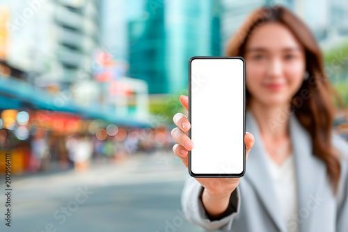 Young woman holding smartphone mockup with blank screen in city street