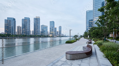 Minimal riverside promenade with sculptural benches and glass towers in pale morning light landscape scenery