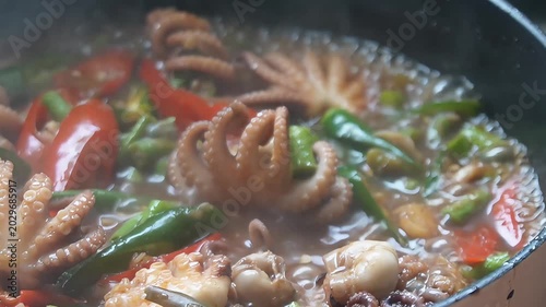 Close-up of spicy stir-fried baby octopus with red and green chili peppers cooking in a hot pan, authentic Asian seafood dish