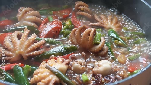 Close-up of spicy stir-fried baby octopus with red and green chili peppers cooking in a hot pan, authentic Asian seafood dish