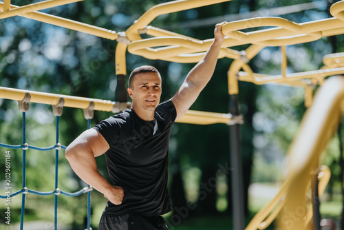 Canvas Print A fit man rests on yellow monkey bars at an outdoor fitness course