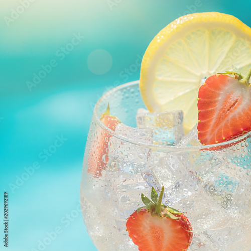 Refreshing Lemonade Cocktail with Strawberries and Ice in Glass Against Blurred Aqua Background
