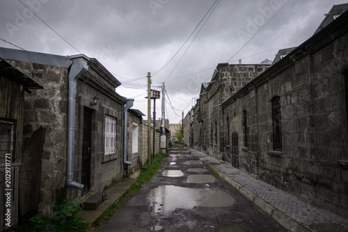 Weathered stone houses flank damp alley under heavy clouds