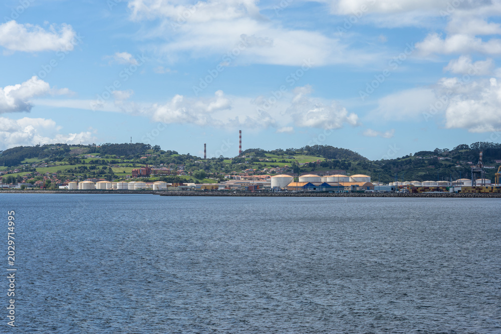 Fototapeta premium Industrial harbor landscape in Gijon, Northern Spain, showing cargo port facilities, fuel reservoirs, and coastal scenery
