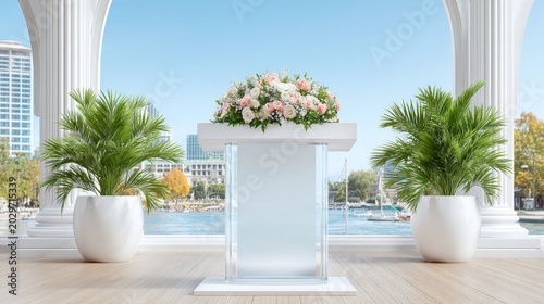 a modern, white podium decorated with a floral arrangement of pink and white flowers, flanked by two potted palm plants on a balcony overlooking a city waterfront.