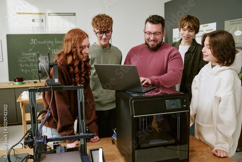 Bild auf Leinwand Teenagers with male teacher reviewing laptop beside 3D printers in classroom, le