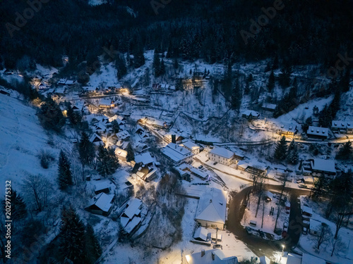 Aerial view of the snow-covered historic village of Spania Dolina with illuminated houses nestled in a dark mountain valley at night, Spania Dolina, Banska Bystrica Region, Slovakia.