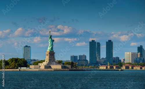 Statue of Liberty with Manhattan skyline under blue sky and clouds, iconic New York landmark view.