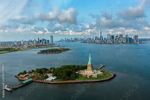 Schilderij op canvas Aerial view of the Statue of Liberty with Lower Manhattan skyline and dramatic clouds over New York Harbor