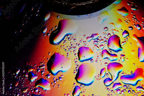 Abstract neon water drops on iridescent compact disc texture. Conceptual psychedelic background of liquid metal, rainbow light reflections on music CD, retro futurism and synthwave technology  