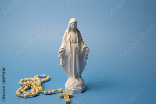 Fotografie Virgin Mary statue with rosary and cross on blue background, studio shot, select