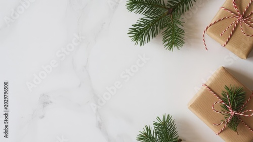 Gifts wrapped in brown paper with twine and pine branches on a white marble surface for Christmas featuring holiday, presents, festive