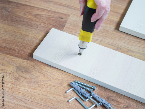 Fotografie Hand tightening a screw into a white wooden panel with a manual screwdriver clos