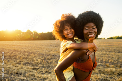 Quadro su tela Beautiful african mom and daughter in a sunflowers field at sunset