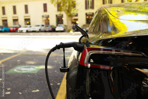 EV charging station power cable handle plugged in for refueling electric vehicle outdoors.