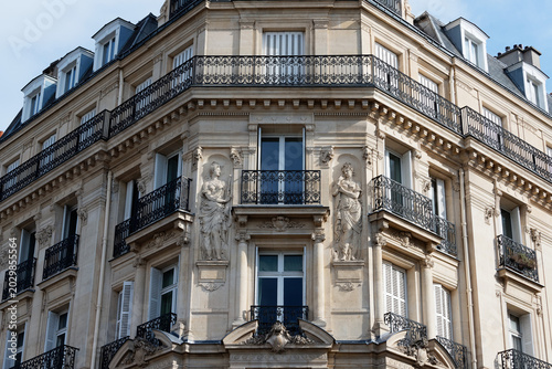Elegant corner of a classic Haussmann-style apartment building on Quai Voltaire, Paris, featuring two finely carved allegorical stone figures in draped robes .