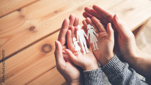 Protective hands gently holding paper cutout family figures showing support and care for community and loved ones.