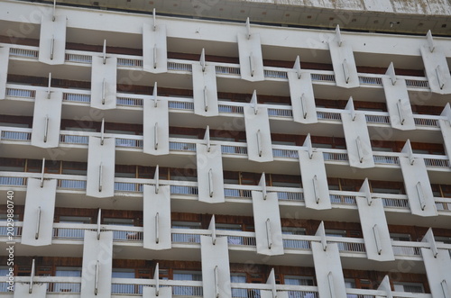 A geometric facade of a Soviet modernist building featuring a repetitive pattern of white concrete balconies and decorative elements. Landmark of brutalist architecture in the Caucasus