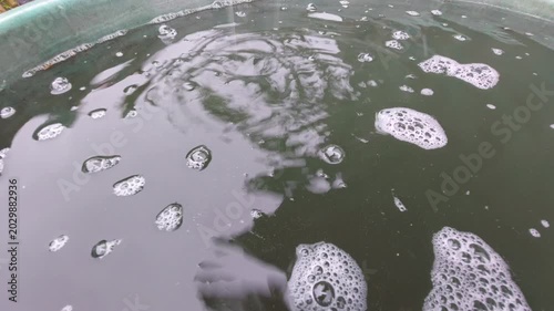 Raindrops falling into a water butt barrel creating ripples and bubbles close up