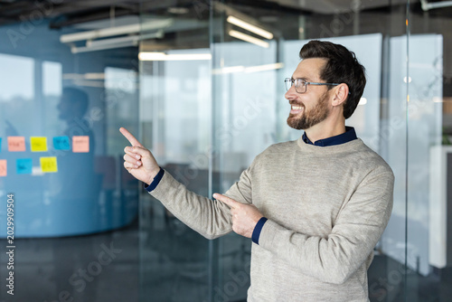 Konstfotografi Smiling businessman presenting to the side, pointing with both hands at an unsee