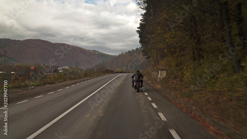 Biker riding motorcycle on mountain road during autumn