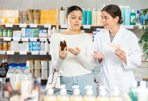 Foto Attentive middle-aged woman choosing syrup while female pharmacist giving offer