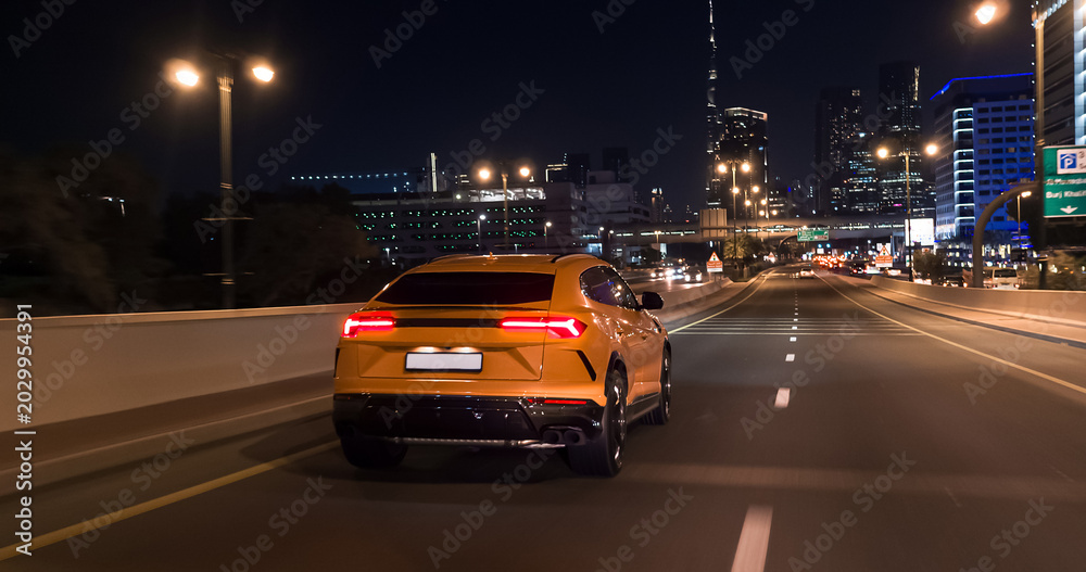 Obraz premium Yellow luxury suv driving on dubai highway at night