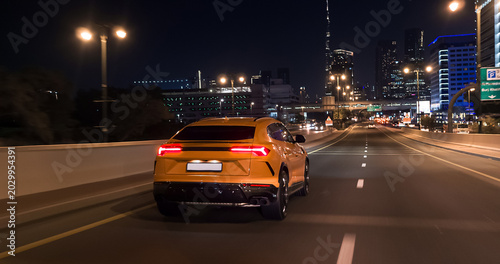 Quadro su tela Yellow luxury suv driving on dubai highway at night