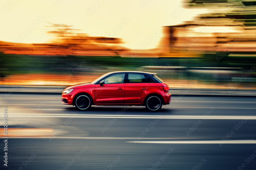 Fototapeta premium Red car driving fast with motion blur at sunset