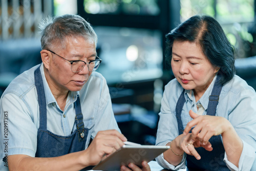 Senior asian restaurant couple analyzing sales data on tablet managing income expense teamwork financial planning collaboration cooperation cafe small business management lifestyle concept