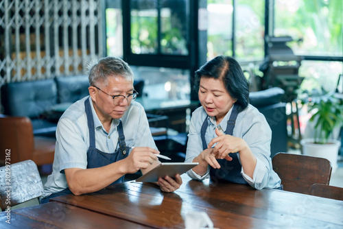 Asian senior restaurant owners checking expense report on tablet managing finance teamwork collaboration communication family small business cooperation budget planning professional cafe concept