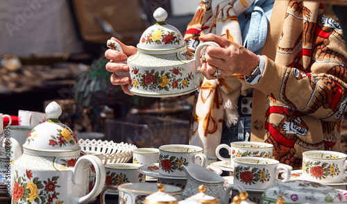 Foto Woman holding decorative porcelain teapot while examining vintage dishware at a