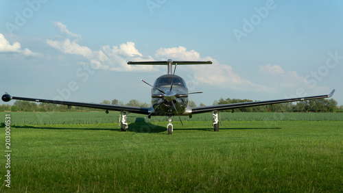 Horizontal photo of a small propeller plane standing on the grass at the airport