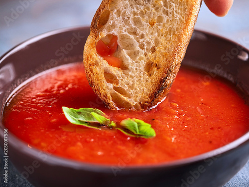 Piece of toasted sourdough bread being dipped into a bowl of fresh homemade tomato soup