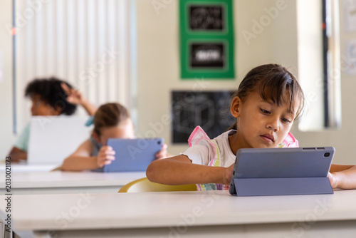 Tableau sur toile Diverse child classmates using tablets in classroom at white desks with gray fol