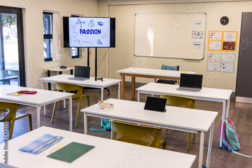 Empty classroom showing white tables, mustard chairs, laptops, tablet, monitor reading PASSION