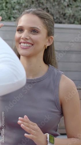 Vertical video: Exchanging high-five, tank-top woman meeting friend entering left on patio, watch