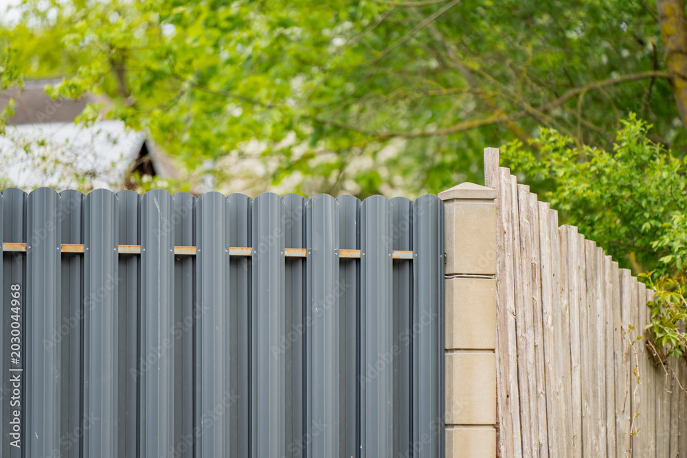 Fototapeta premium Perimeter boundary fencing upgrade showing a new grey metallic corrugated picket section replacing an old rustic wooden plank fence line on a residential property