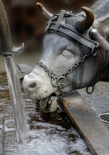 Canvas Print Close up of a cow sculpture drinking water at a traditional trough with flowing