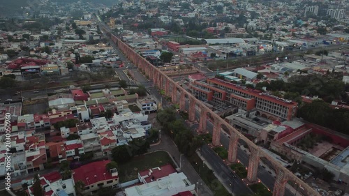 Aerial dolly in shot approaching historic Aqueduct of Queretaro with colonial urban landscape and moving traffic in Santiago de Queretaro Mexico during evening light