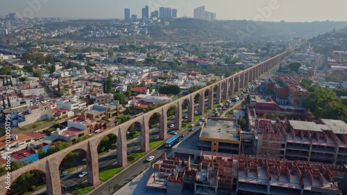 Tilt up aerial shot showing traffic city skyline mountains and Aqueduct of Queretaro in Santiago de Queretaro Mexico during sunny afternoon cinematic urban panorama