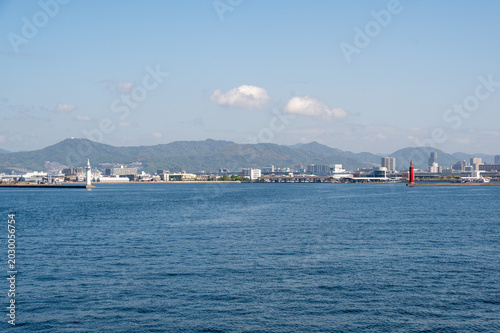 Scenic view of Hiroshima harbor with the white Ujina Lighthouse on a lush green peninsula, Japan