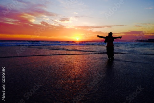 Bild auf Leinwand Mulher com braços abertos em meio a ondas rasas num por do sol com vento soprand
