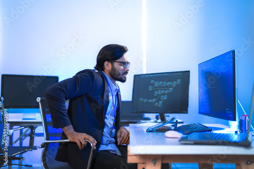 Obraz na plátně Focused Indian software engineer analyzing database codes and advanced microprocessor unit scripts on multiple desktop screens inside a tech laboratory