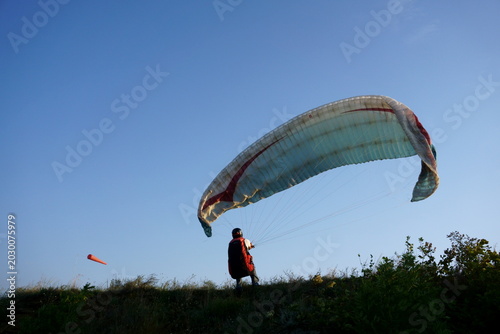 Foto Paraglider pilot preparing for takeoff on a grassy hill against clear blue sky