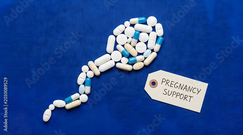 White pills arranged in spermatozoa shape on blue background with pregnancy test label. Generative AI image